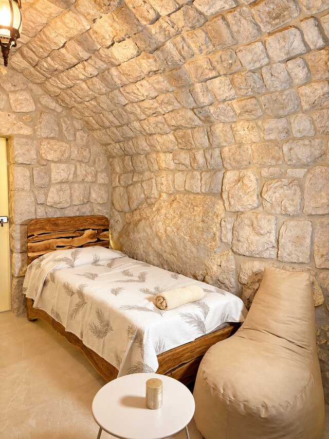 One of the two single beds in Gemelli, raw timber frame against the stone wall.