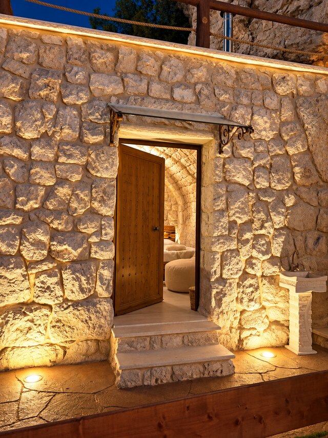 Gemelli's entrance at night, a timber door set into the stone facade at the lower end of the property.