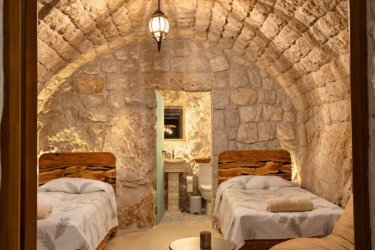 Gemelli: two matching beds facing each other under the vaulted stone ceiling, the ensuite door open beyond them.