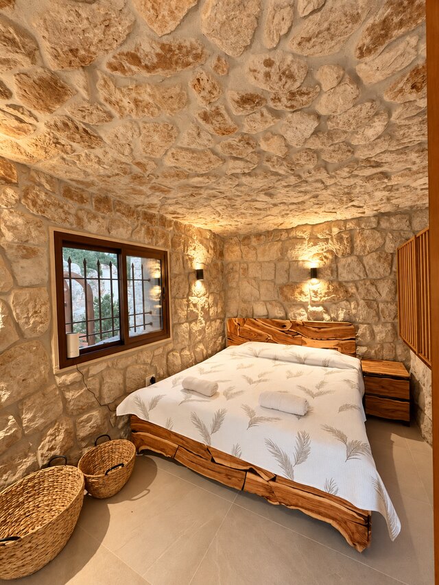 The bed in La Grande, raw timber frame against the stone wall beneath the window.