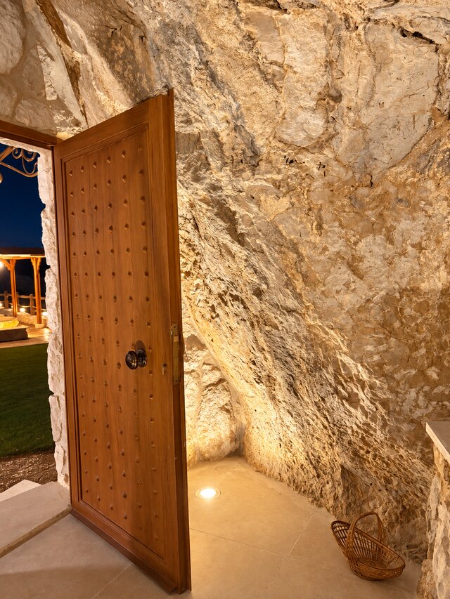 The timber door into La Grotta, set into the rock face with the terrace lights visible outside at night.