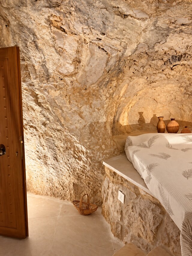 A wider view of the La Grotta bed niche, with woven baskets and clay pottery on the rock ledge beside it.