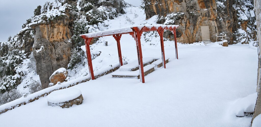 The Cap de Douma terrace under deep snow, the red pergola and stone benches buried beneath the limestone rock face.