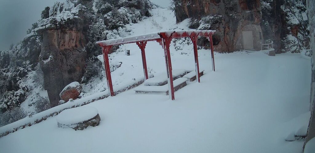 Snow banked across the Cap de Douma terrace, weighing on the red pergola with the limestone cliffs behind.